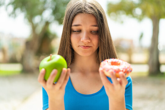 Teenager girl at outdoors holding apple and donut