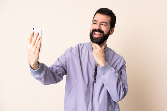 Caucasian man with beard wearing a jacket over isolated background making a selfie
