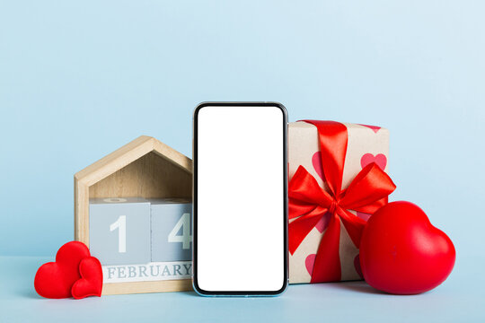 mobile phone with blank screen on colored background with hearts, calendar and gift box, valentine day 14 february concept perspertive view flat lay
