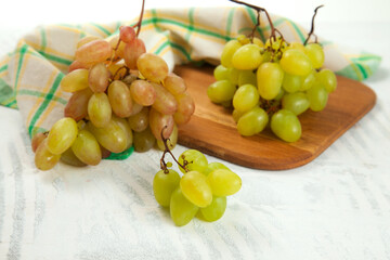 Cutting board with bunch of organic green and pink grapes on white wooden background..