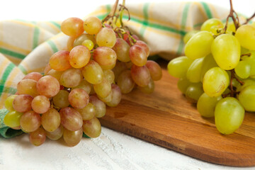 Cutting board with bunch of organic green and pink grapes on white wooden background..