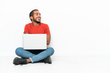 Young Ecuadorian man with a laptop sitting on the floor isolated on white background happy and...