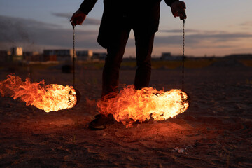 Close up of unrecognizable man holding flaming poi in dark outdoors during fire show performance,...