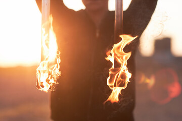 Close up of flaming fire rods with lens flare, unrecognizable fire show performer outdoors, copy...