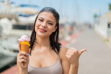 Young pretty woman with a cornet ice cream at outdoors pointing to the side to present a product