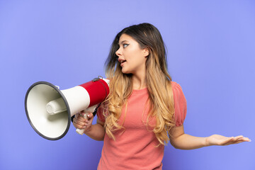 Young Russian girl isolated on blue background holding a megaphone and with surprise facial...