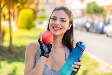 Young pretty sport woman at outdoors with an apple and with a bottle of water