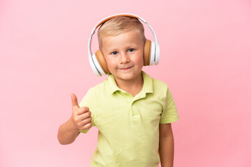 Little Russian boy isolated on pink background listening music with a mobile making rock gesture