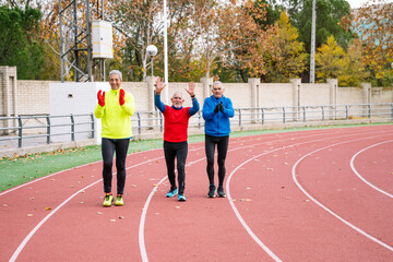 Obraz premium Three joyful seniors engage in fitness on a track, exuding vitality and happiness. Active lifestyle concept for elderly people.