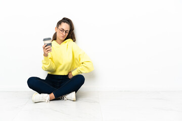 Young woman sitting on the floor holding a take away coffee with sad expression