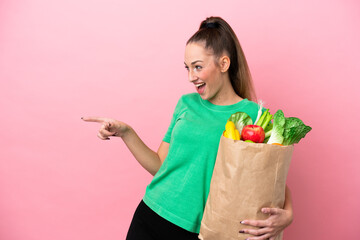 Young woman holding a grocery shopping bag pointing finger to the side and presenting a product