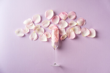 Obraz premium Pink rose petals in champagne flute on purple background