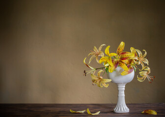 yellow lily in ceramic white vase on wooden table