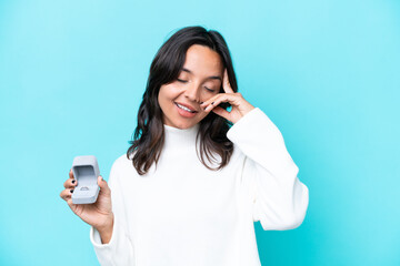 Young hispanic woman holding a engagement ring isolated on blue background smiling a lot