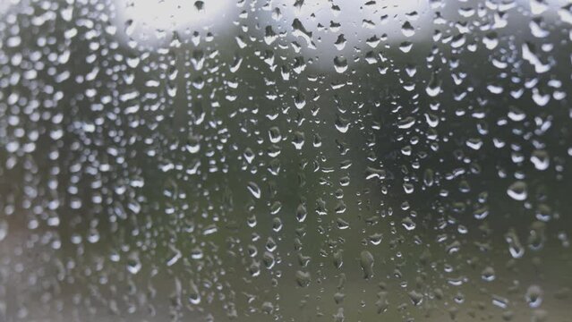 A view outside a cabin glass window with large raindrops on it and an out of focus forest in the background