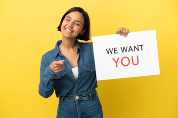 Young mixed race woman isolated on yellow background holding We Want You board and pointing to the...