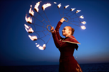 Full length portrait of young woman dancing with fire fans against night sky