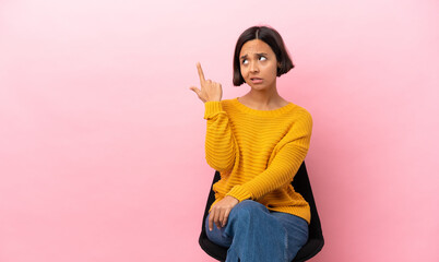 Young mixed race woman sitting on a chair isolated on pink background making the gesture of madness...