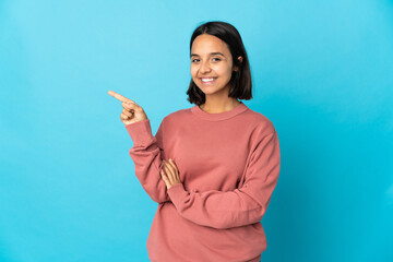 Young latin woman isolated on blue background pointing finger to the side