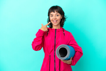 Obraz premium Young girl going to yoga classes while holding a mat isolated on blue background giving a thumbs up gesture