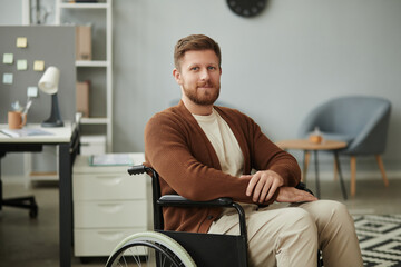 Portrait of bearded man with disability smiling at camera in office setting, copy space