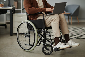 Fototapeta premium Close up of unrecognizable man with disability using laptop sitting in wheelchair at office, copy space