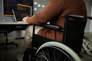 Close up of unrecognizable man with disability using wheelchair while working at desk in office,...