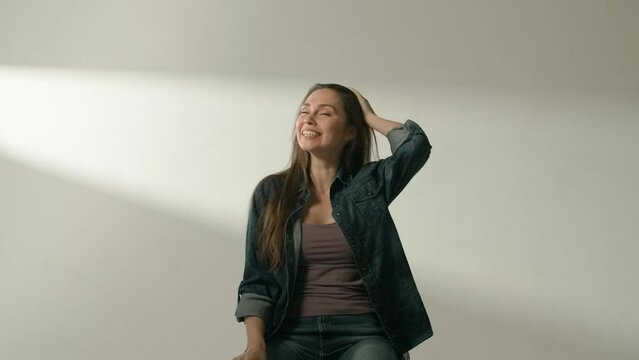 Portrait of attractive female model in positive mood. Brunette woman in casual clothing sitting in the studio and laughing taking a breathe in.