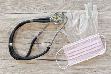 Surgical mask, stethoscope and medical gloves layed out on wooden background - 698572907
