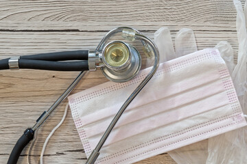 Surgical mask, stethoscope and medical gloves layed out on wooden background - 698572932