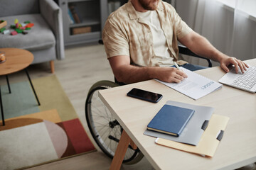 Close up of unrecognizable man with disability working with financial documents at home office workplace, copy space