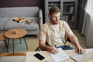 Portrait of bearded man with disability working with financial documents and using laptop at home office workplace, copy space