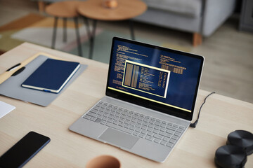 High angle background image of open laptop with code lines on screen at home office desk