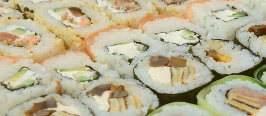 Close-up of a lot of sushi rolls with different fillings lie on a wooden surface. Macro shot of cooked classic Japanese food with a copy space.