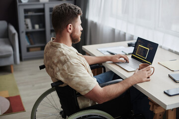 Side view portrait of bearded man with disability using computer while working from home in IT career