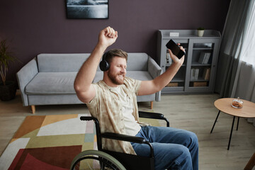 High angle portrait of carefree young man with disability dancing in wheelchair at home and listening to music, copy space
