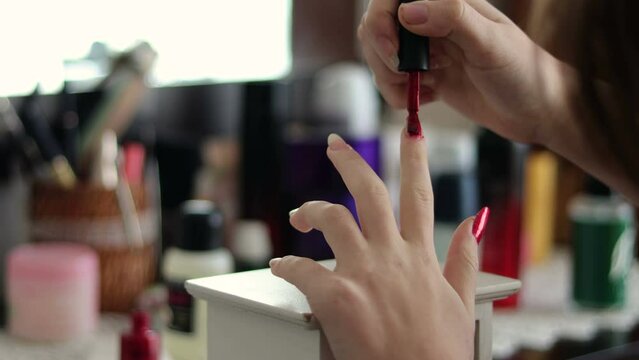 Young girl puts red nail polish on her long nails at home