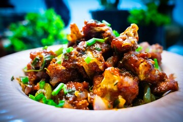 Gobi Manchurian Homemade, Indo Chinese fried Cauliflower florets, Gobi Manchurian is Indian Chinese cuisine dish with cauliflower, tomatoes, onion, soy sauce in white plate selective focus. - obrazy, fototapety, plakaty