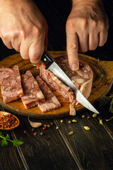Slicing brawn on a cutting board with a knife in the hands of a cook. Quick snack idea with headcheese with aromatic spices
