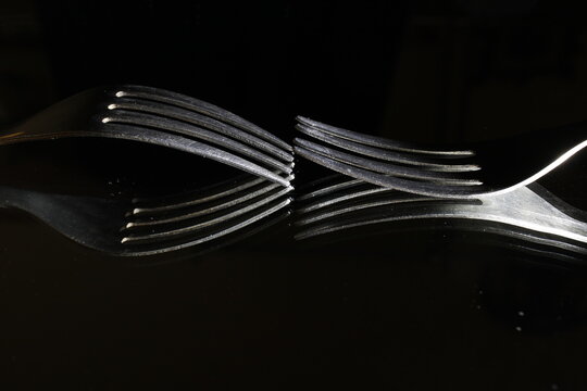 Tenedores de acero de cuatro puntas como utensilios de comida, reflejados en la superficie  formando ondas y curvas abstractas, crean un original diseño culinario sobre un fondo negro