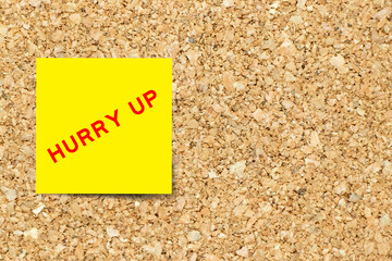 Yellow note paper with word hurry up on cork board background with copy space