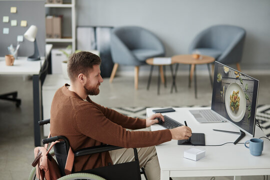 Side view portrait of bearded man with disability editing photos at office workplace and using pen tablet, copy space