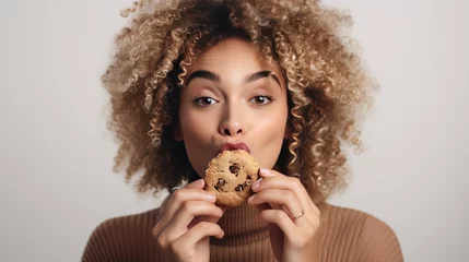 Fotobehang Tasty Vice. Woman Savoring Unhealthy Chocolate-Infused Cookie. Caloric Delight. Woman Nibbles on Unhealthy Chocolate Chip Cookie. This kind of snack is bad for your health © Yauhen