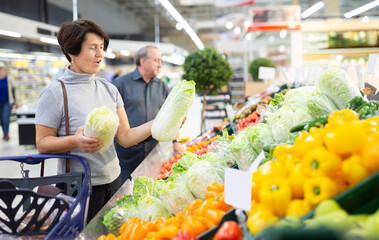 Mature female customer selects savoy cabbage with interest in grocery department of supermarket