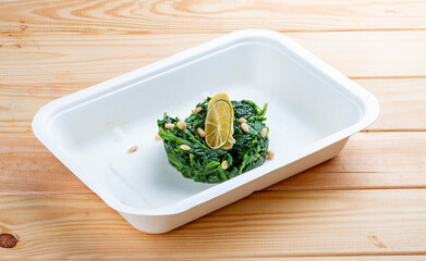 Braised spinach with pine nuts. Healthy food. Takeaway food.  On a wooden background.