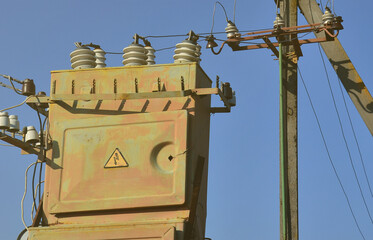 Old and obsolete electrical transformer against the background of a cloudless blue sky. Device for...