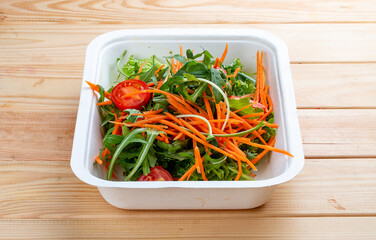 Salad mix (greens, carrots and cherry tomatoes). Healthly food. Takeaway food. On a wooden background.