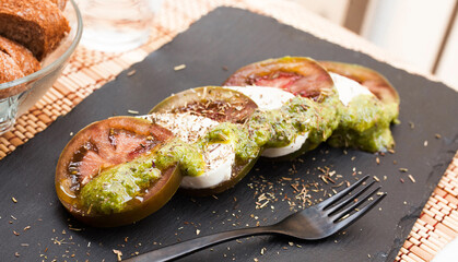 Caprese salad with mozzarella, black tomatoes and pesto on black stone plate