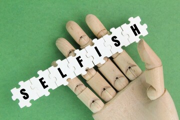 wooden hand and white puzzle with the word selfish. the concept of self-importance