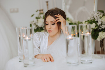 A beautiful brunette bride with a tiara in her hair is getting ready for the wedding in a beautiful robe in boudoir style. Close-up wedding portrait, photo.